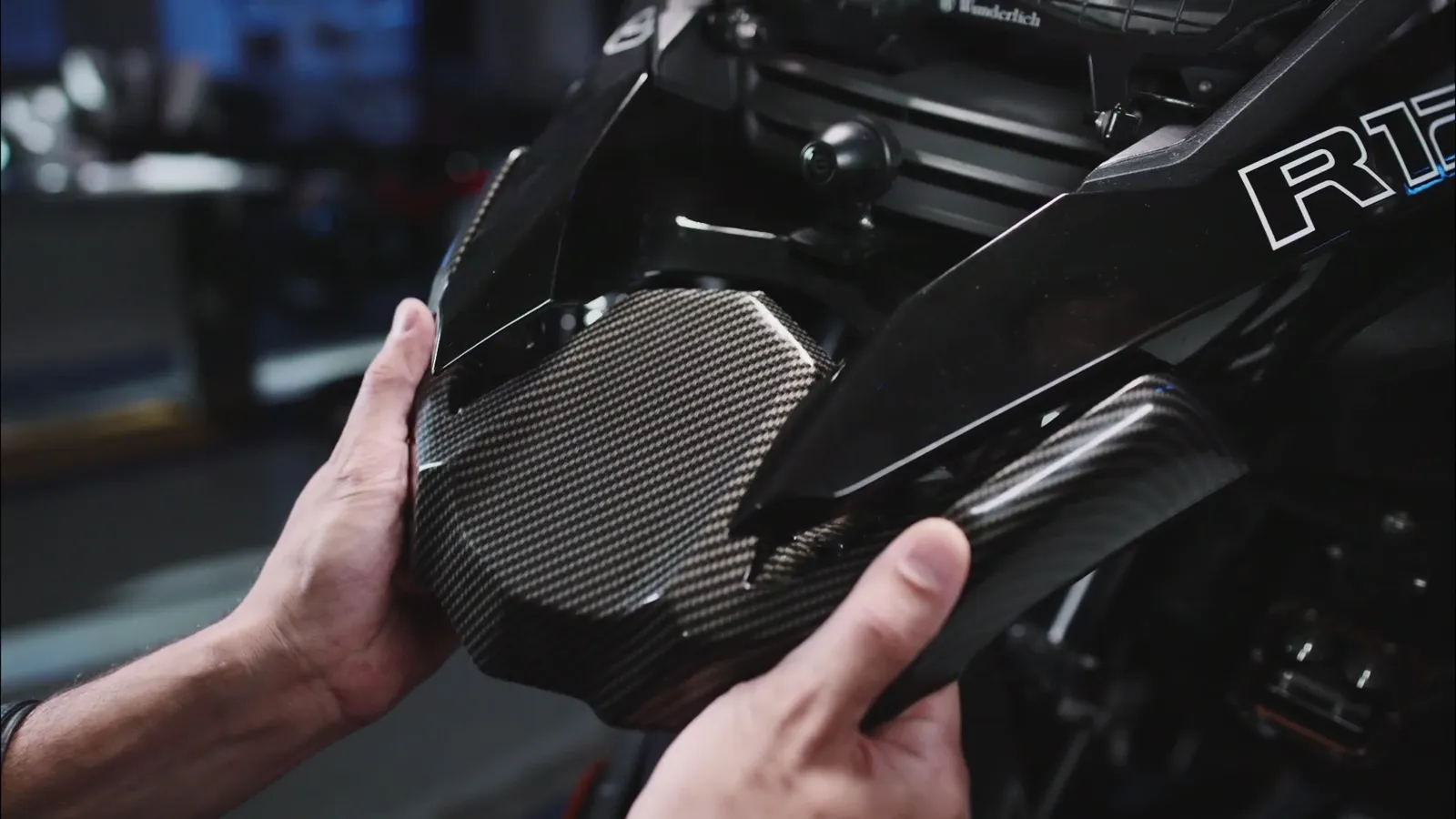 Mãos encaixando uma peça de fibra de carbono preta em uma moto